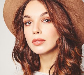 Portrait of young stylish laughing girl model in gray casual summer clothes in brown hat with natural makeup isolated on gray background. Looking at camera Portrait of young stylish laughing girl model in gray casual summer clothes in brown hat with natural makeup isolated on gray background. Looking at camera